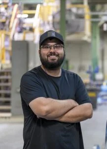 man standing in a manufacturing plant with his arms crossed and smiling