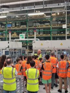 group of people in orange and yellow safety vests getting a tour of a manufacturing facility