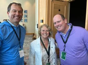 3 people standing together smiling with badges around their necks at a tradeshow