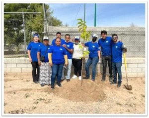group of people wearing blue shirts posing with a newly planted tree