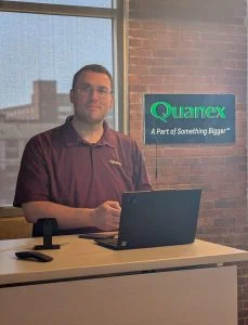 man standing in an office with red brick walls working on a laptop