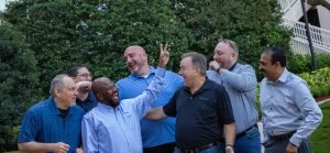 Group of 7 men of different nationalities laughing an giving bunny ears to each other in an outside environment